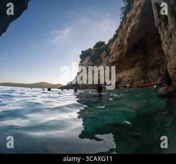 Dubrovnik, Kroatien - 12. September 2023: Kajakfahrer halten bei einer Tour bei Sonnenuntergang an einer Höhle. Die Leute schwimmen und entspannen sich, bevor die Tour fortgesetzt wird. Stockfoto