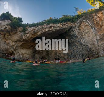Dubrovnik, Kroatien - 12. September 2023: Kajakfahrer halten bei einer Tour bei Sonnenuntergang an einer Höhle. Die Leute schwimmen und entspannen am Strand. Stockfoto