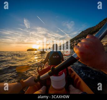 Dubrovnik, Kroatien - 12. September 2023: Kajakfahrer paddeln auf einer geführten Tour in den Sonnenuntergang. Sie genießen die wunderschöne Landschaft und das ruhige Wasser. Stockfoto