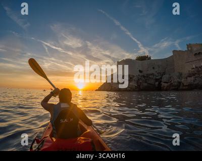 Dubrovnik, Kroatien - 12. September 2023: Ein Kajak paddelt in den Sonnenuntergang während einer Führung entlang der Küste in der Nähe der alten Stadtmauern. Stockfoto