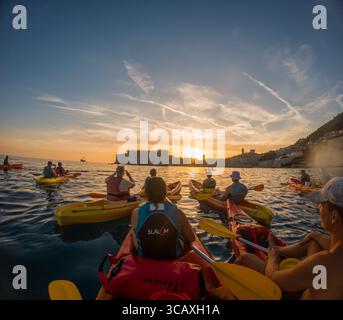 Dubrovnik, Kroatien - 12. September 2023: Kajakfahrer paddeln auf einer geführten Tour in Richtung Sonnenuntergang und genießen die malerische Aussicht auf die historischen Stadtmauern. Stockfoto