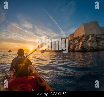 Dubrovnik, Kroatien - 12. September 2023: Kajakfahrer paddeln während einer Tour bei Sonnenuntergang entlang der Adria, mit den Stadtmauern im Hintergrund. Stockfoto