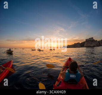 Dubrovnik, Kroatien - 12. September 2023: Kajakfahrer genießen eine Tour bei Sonnenuntergang in der Nähe der Stadtmauern. Stockfoto