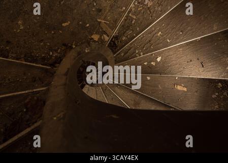 Blick von oben auf eine staubige, verlassene Wendeltreppe in einem alten, verfallenen Gebäude mit rustikalen Holztreppen und Trümmern, die herum verstreut sind Stockfoto