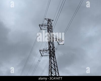 Stromkabel und Strommasten vor grauem bewölktem Himmel. Stockfoto