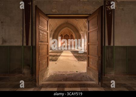Blick durch offene Holztüren in ein verlassenes, verfallenes Kapelleninnere mit Bogendecke und Altar in einem französischen Kloster Stockfoto
