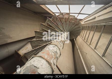 Rostige Wendeltreppe in verlassenem Industriebau mit abblätternder Farbe und Metallstruktur Stockfoto
