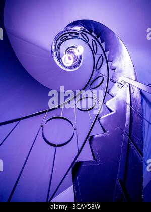 Abstrakte Wendeltreppe mit geometrischem Metallgeländer und moderner Beleuchtung in coolem Blauton Stockfoto
