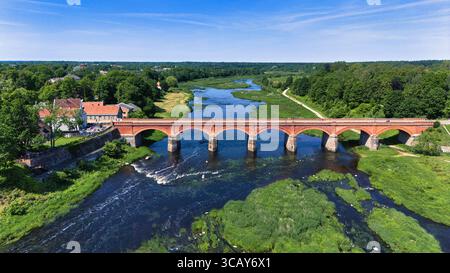 Drohnenaufnahme von Kuldīga ikonischer Brücke aus roten Ziegeln über den Fluss Venta - Lettlands verstecktes Juwel Stockfoto