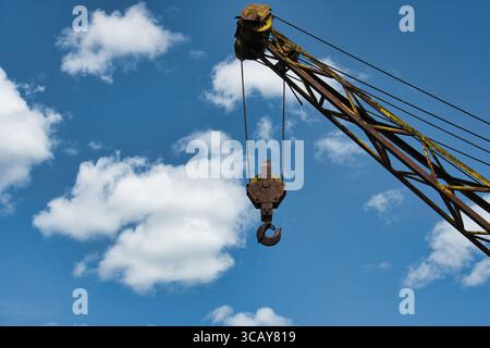 Rostiger Industriekranhaken gegen blauen Himmel mit Wolken - Vintage-Baumaschinen Stockfoto