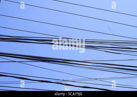 Schwarze Hochspannungsleitungen erstrecken sich über einen klaren blauen Himmel. Stockfoto