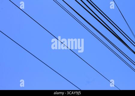 Schwarze Hochspannungsleitungen erstrecken sich über einen klaren blauen Himmel. Stockfoto