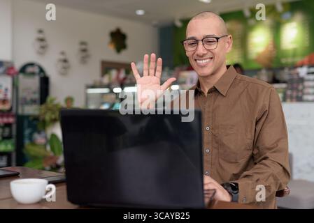 Reifer hispanischer Mann mit Laptop im Café im Haus, mit Brille und Button-Down-Hemd. Selbstbewusster und fokussierter Ausdruck. Fernarbeit, Freiberufler, t Stockfoto