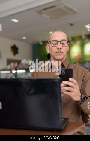Reifer hispanischer Mann mit Laptop im Café im Haus, mit Brille und Button-Down-Hemd. Selbstbewusster und fokussierter Ausdruck. Fernarbeit, Freiberufler, t Stockfoto