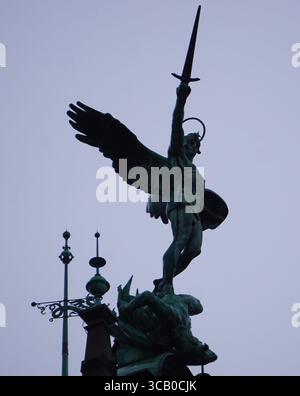 Vertikale Nahaufnahme einer Michael-Statue mit einem Schwert auf dem Wahrzeichen-Dach des Hamburger Rathauses vor grauem und bewölktem Himmel Stockfoto