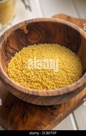 Roher Couscous in einer Schüssel auf einem hölzernen Schneidebrett. Stockfoto