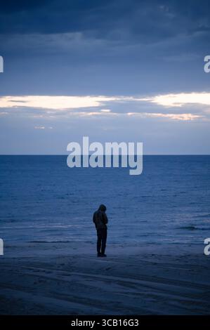 Eine Person, die an einem bewölkten Abend kurz nach Sonnenuntergang am Ufer des Lake Michigan steht Stockfoto