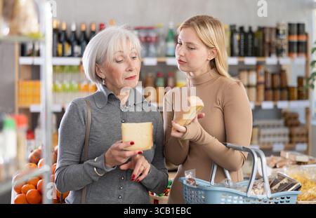 Die Erwachsene Tochter hilft älteren Müttern, im Supermarkt leckeren Käse zu wählen Stockfoto
