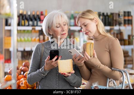 Die ältere Mutter und ihre Erwachsene Tochter scannen zusammen einen QR-Code auf einem Käseetikett, um das Verfallsdatum zu überprüfen Stockfoto