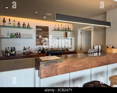 Moderne Hotelbar mit Holztheke, hinterleuchteten Regalen mit Flaschen, Glaswaren und warmer Beleuchtung im Lince Nordeste Country Hotel. Stockfoto