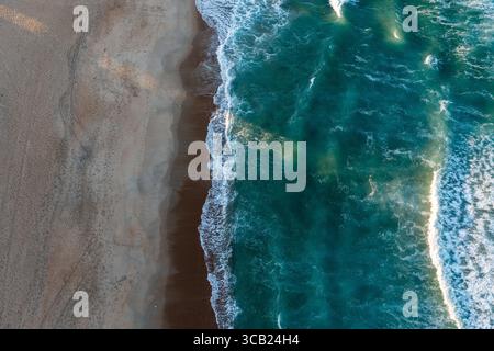 Aus der Vogelperspektive von oben auf das wunderschöne blaue Meer Wasser mit einem leeren, einsamen Strand bei Sonnenuntergang Stockfoto