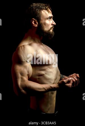 Ein muskulöser Mann mit Bart beugt seine Arme und zeigt seine Körper vor schwarzem Hintergrund. Stockfoto