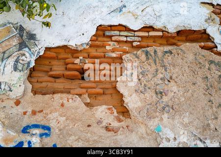 Freiliegender roter Backstein mit gebrochenem Stuck an der Wand eines Gebäudes im Stadtteil La Paz, BCS Mexiko. Stockfoto
