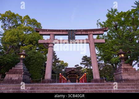 Ein ruhiger Blick auf ein traditionelles japanisches Torii-Tor an einem Tempeleingang, umgeben von üppigem Grün, das während der Abenddämmerung erfasst wurde, Kyoto, Japan Stockfoto