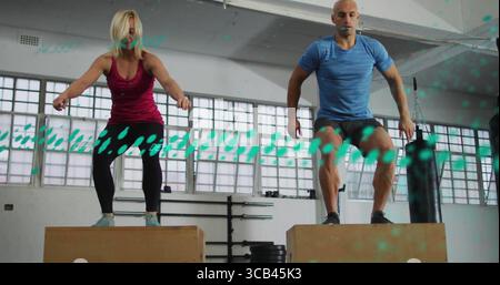 Springende Fitnesspartner auf Holzboxen in Sportbekleidung im Fitnessstudio mit Langhantelablage Stockfoto