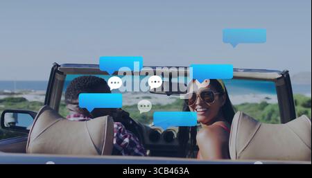 Ein lächelndes Paar mit Sonnenbrille plaudert in einem Cabrio auf der Küstenstraße mit Chat-Blasen Stockfoto