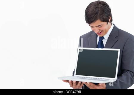 Geschäftsmann im Anzug, der im Studio steht und einen Laptop hält, mit einem leeren Bildschirm, der herunterlächelt, Kopierraum Stockfoto