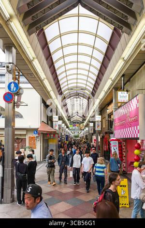 Lebhafte Szene mit Menschen, die durch die Einkaufsstraße Teramachi Kyogoku in Kyoto laufen. Das Bild zeigt verschiedene Geschäfte, kulturelle Vielfalt und Japan Stockfoto