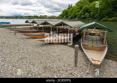 Mehrere traditionelle Holzboote mit grünen Dächern liegen entlang des Katsura River an einem Kiesstrand, Ukyo Ward, Kyoto Stockfoto