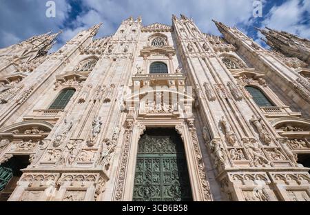 Flacher Blick auf die Vorderfassade an einem sonnigen, klaren Tag mit traumhaft blauem Himmel und weißen, geschwollenen Wolken. Im Duomo in Mailand, Italien. Stockfoto