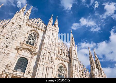 Flacher Blick auf die Vorderfassade an einem sonnigen, klaren Tag mit traumhaft blauem Himmel und weißen, geschwollenen Wolken. Im Duomo in Mailand, Italien. Stockfoto