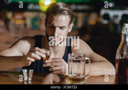 Mann, der allein im Pub sitzt. Mann mit Alkohol. Trauriger Kerl in der Bar. Der Typ in der dunklen Bar. Alkoholproblem. Einsamer Mann trinkt Whiskey im Restaurant. Depressiver Mann Stockfoto