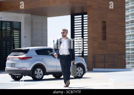 Reicher Geschäftsmann in der Nähe eines Luxusautos. Reicher Geschäftsmann im Anzug draußen. Erfolgreicher reicher Geschäftsmann in der Stadt. Geschäftsmann mit selbstbewusstem Blick Stockfoto