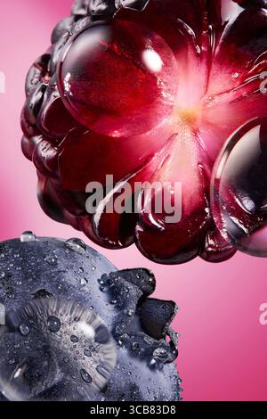 Nahaufnahme von saftiger Brombeere und Blaubeere mit Wassertropfen auf rosa Hintergrund, Makrofoto von brombeere mit Wassertropfen auf rosa Hintergrund. Stockfoto