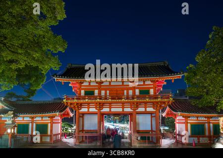 Foto von einem wunderschön beleuchteten Yasaka Jinja Nishiromon Tor bei Nacht mit lebhaften Farben, umgeben von üppigen grünen Bäumen und bietet eine ruhige Atmosphäre Stockfoto