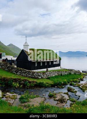 An den ruhigen Ufern der Färöer-Inseln gelegen, bietet eine traditionelle Kirche ein grünes Grasdach, das die üppige Landschaft ergänzt. Funnings Church Stockfoto