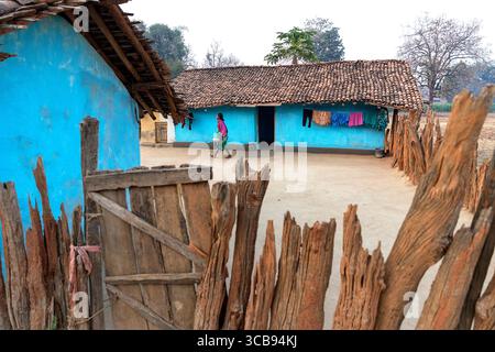 Einheimische Frau, die in einem Haus aus Schlamm in einem abgelegenen Teil indiens spaziert, Zaun aus altem Holz, blaues Haus Stockfoto