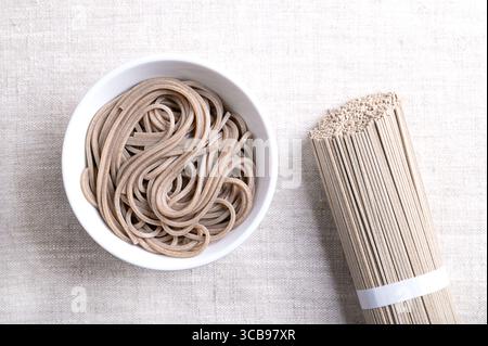 Soba-Nudeln, gekocht und gekühlt, in weißer Schüssel auf Leinengewebe. Dünne japanische Nudeln, die hauptsächlich aus Buchweizenmehl hergestellt werden, wobei Weizenmehl gemischt wird Stockfoto