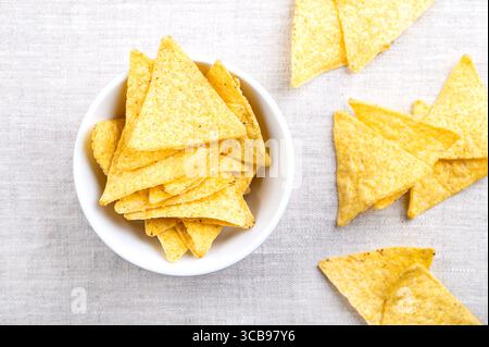 Tortillachips in weißer Schüssel auf Leinen. Klassische, knusprige Snacks aus Maistortillas, in dreieckige Keile geschnitten, in Öl frittiert und gesalzen Stockfoto