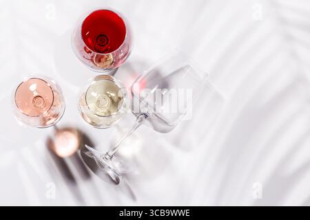 Drei Weingläser gefüllt mit Rot-, weiß- und Rosenwein, anmutig auf einem hellen, minimalistischen Hintergrund. Eine lebendige Darstellung der Vielfalt der Weine Stockfoto