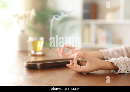 Nahaufnahme einer Frau, die sich beim Yoga-Verbrennen von Räucherstäbchen auf einem Holztisch zu Hause entspannt Stockfoto