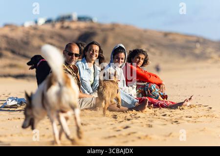 Gruppe von Freunden, die mit ihren Hunden am Strand meditieren, nach einem spirituellen Rückzug, genießen die Ruhe und Verbindung mit der Natur Stockfoto