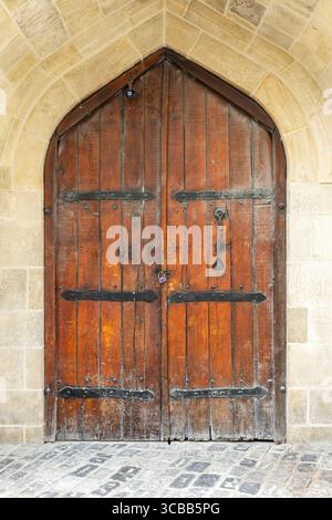 Alte Holztür mit Eisenscharnieren und einem Vorhängeschloss in einem Steinrahmen mit Bogendesign. Vorderansicht, Hintergrundfotostruktur Stockfoto