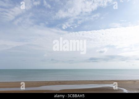 Friedliche Landschaft mit einer sandigen Küste, ruhigem Meer und einem Himmel voller flauschiger weißer Wolken, die ein entspannendes und ruhiges Küstennähe bieten Stockfoto