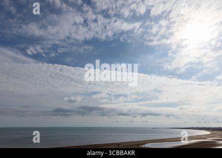 Küstenlandschaft mit Sandstrand, ruhigem Meer und blauem Himmel, gefüllt mit flauschigen weißen Wolken, bietet ein entspannendes und ruhiges Küstenambiente. Stockfoto
