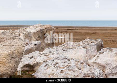 Eine ruhige Küstenlandschaft mit großen Felsen, einer sandigen Küste und einem ruhigen Blick auf das Kaspische Meer unter weichem Himmel Stockfoto